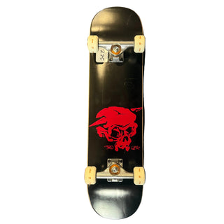 A black skateboard viewed from above on a scratched gray metal floor, featuring a large red skull graphic and small red text on the deck.