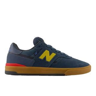 A New Balance skate shoe in navy blue suede and mesh, featuring a prominent yellow 'N' logo on the side, a red stripe on the midsole, and a brown gum rubber sole, shown against a plain white background.
